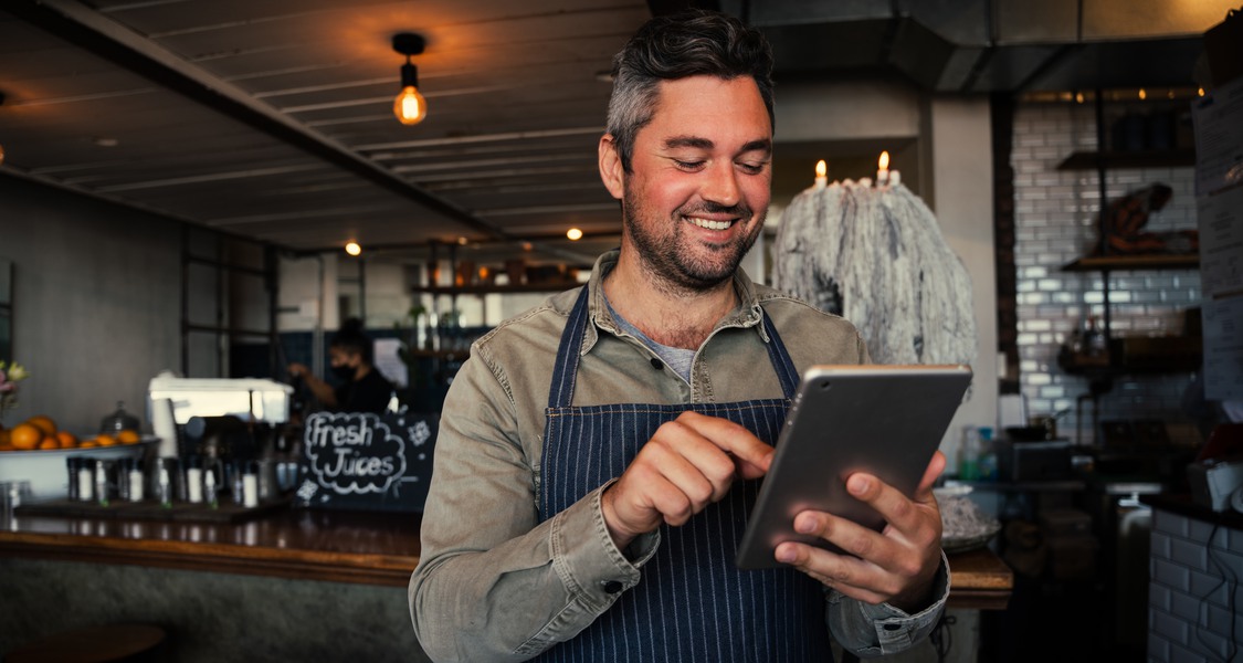 Bild: Manlig servitris ler när han ser något kul i sin iPad.