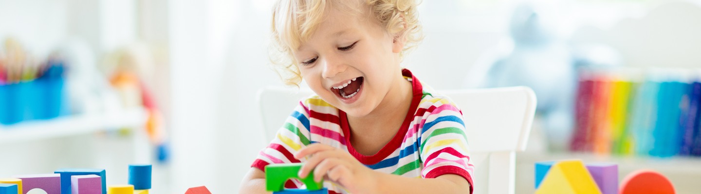 Kid playing with colorful toy blocks. Little baby building tower of block toys. Educational and creative toys and games for young children. Baby in white bedroom with rainbow bricks. Child at home.