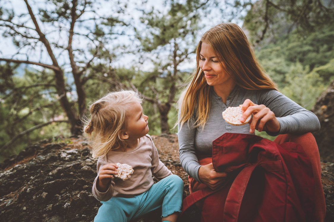 Family lifestyle mother and daughter child outdoor in forest on picnic eating rice cookies travel vacations together with kid