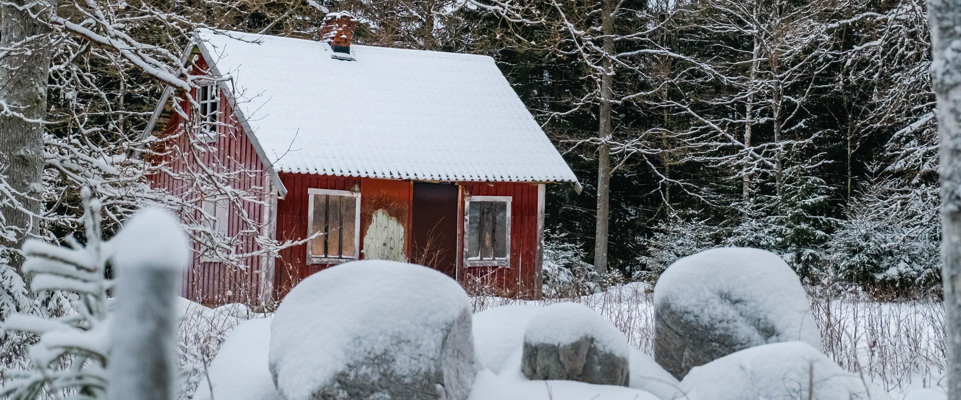 Bild föreställande en liten röd stuga i ett snölandskap