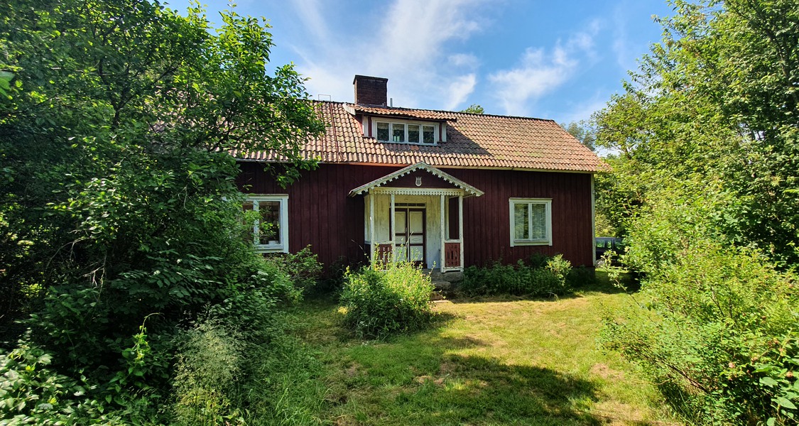 Bild föreställande äldre rött hus med veranda och snickarglädje med grönska omkring