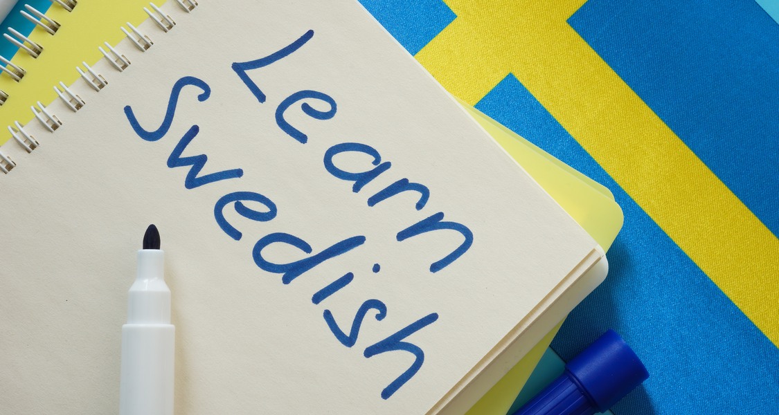 Bild: Ett skrivblock med texten Learn Swedish ligger ovanpå en svensk flagga.