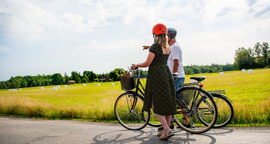 En kvinna och en man har stannat till med sina cyklar vid Hylteleden. Kvinnan pekar på något i horisonten.