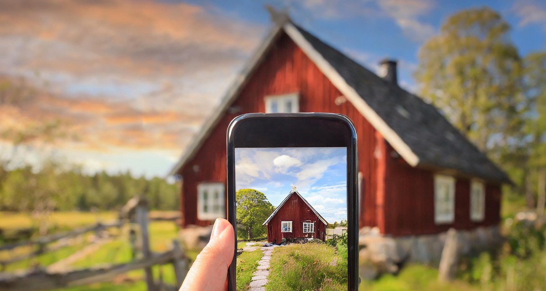 Bild: En mobil hålls upp för att ta kort av ett gammalt rött hus på landsbygden
